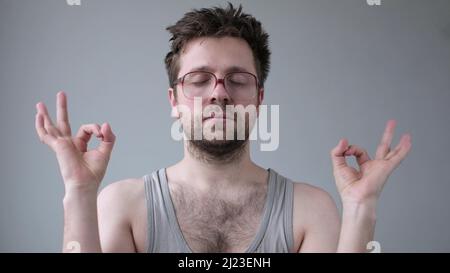 Concentrated bearded man in huge glasses meditates, tries to relax keeps fingers together. Meditation and relax concept. Stock Photo