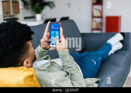 Young latin american man using IOT app on smart phone at home Stock Photo