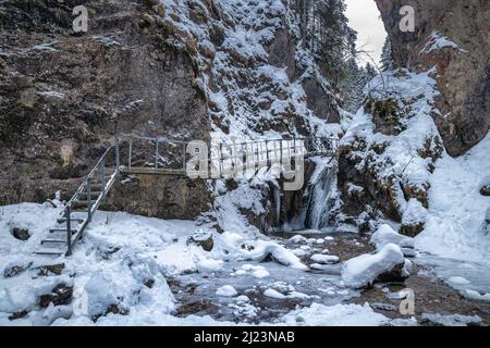 Snowy winter landscape with a bridge on tourist trail through a narrow gorge with wild stream. The Mala Fatra national park in Slovakia, Europe. Stock Photo