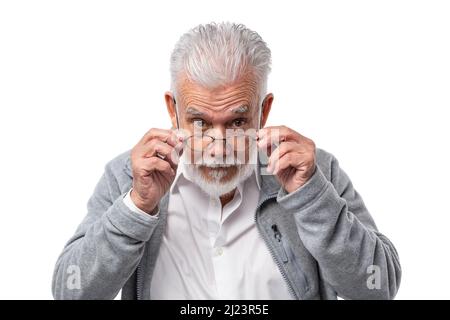 An elderly stylish man in glasses with a beard and gray hair looks from under forehead and holds glasses with his hands.  Stock Photo