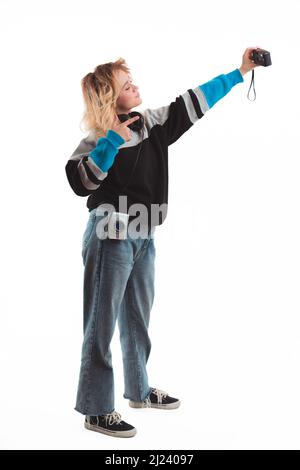 90s-inspired. Blonde-haired caucasian teenage girl taking selfie with her analog camera. Vertical studio shot. Copy space. High quality photo Stock Photo