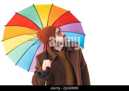 Portrait of young handsome bearded Caucasian man holding a multicoloured umbrella and looking up at the sky weather forecast concept brown casual attire isolated white background studio shot . High quality photo Stock Photo