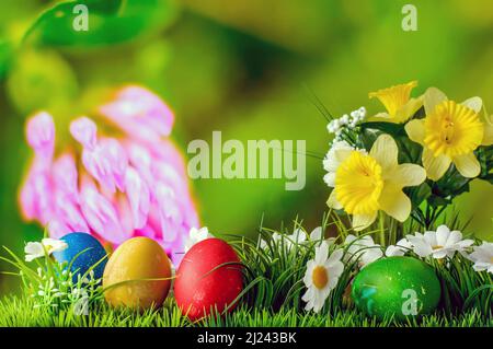 Easter composition, colorful eggs in grass with flowers on a colorful blurry background, still life Stock Photo
