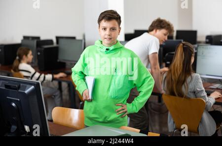 Preteen schoolboy with workbooks in hands standing in computer class Stock Photo