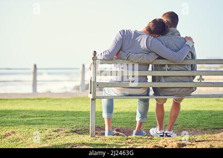Taking in a romantic afternoon. Rearview shot of a young gay couple sitting together on a park bench. Stock Photo