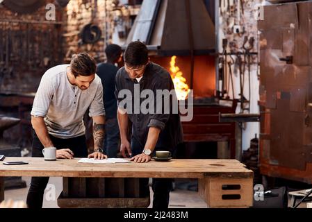 Were working on a huge project together. Cropped shot of two handsome young businessmen working together inside their workshop. Stock Photo