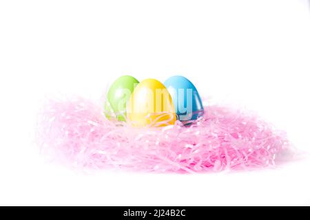 Three colorful Easter eggs on a bed of pink grass on white background Stock Photo