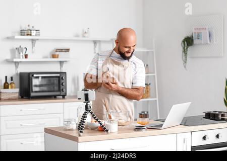 Handsome man making notes while watching cooking video tutorial on laptop in kitchen Stock Photo
