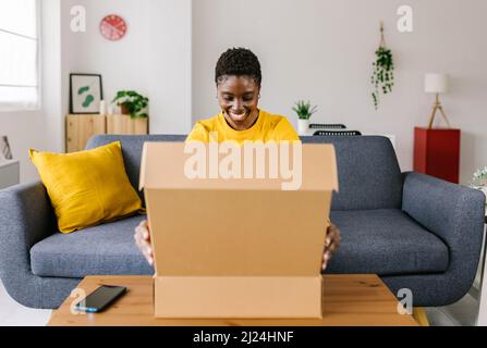 Young woman opening cardboard delivery package after shopping online Stock Photo