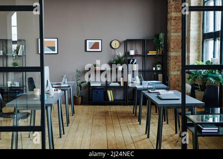 Interior of spacious modern openspace office with computers on desks, shelves with documents and green plants and pictures on wall Stock Photo