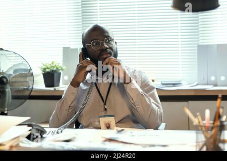 Contemporary male agent of FBI thinking of something while holding phone receiver by ear and talking to colleague on assignment Stock Photo