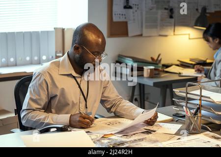 Young FBI agent looking through personal data of suspects in criminal profiles and making notes while analyzing crime circumstances Stock Photo