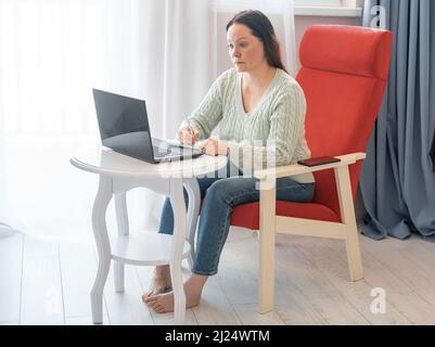 Adult woman taking notes in notebook. woman watches a webinar and writes out important notes for herself. female freelancer writing details on book wh Stock Photo