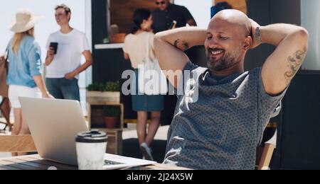 Im so pleased with how this project is turning out. Shot of a businessman sitting and working at a table outside using his laptop. Stock Photo