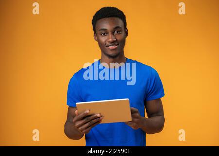 Smiling african guy using digital tablet over yellow background Stock Photo