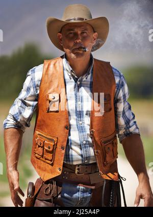 Hes the wrangler of beasts. A mature cowboy outdoors with his gun drawn. Stock Photo