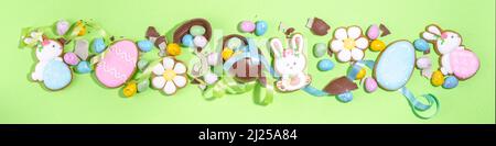 Happy Easter colorful flatlay. Colorful sugared and chocolate Easter eggs, sugar glazed cookies with festive holiday ribbon on light green background Stock Photo