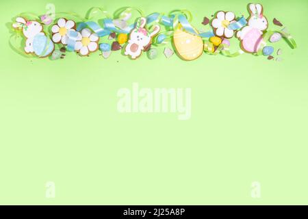Happy Easter colorful flatlay. Colorful sugared and chocolate Easter eggs, sugar glazed cookies with festive holiday ribbon on light green background Stock Photo