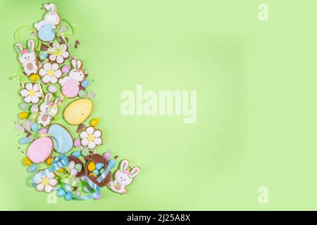 Happy Easter colorful flatlay. Colorful sugared and chocolate Easter eggs, sugar glazed cookies with festive holiday ribbon on light green background Stock Photo