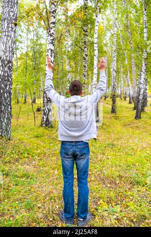 Rear View of a Young Man with Hands Up in the Forest Stock Photo