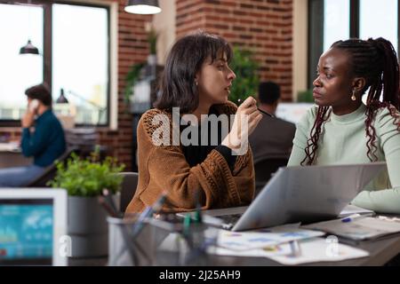 Multiracial group analyzing marketing statistics on laptop computer discussing company strategy during business meeting in startup office. Multiethnic businesspeople brainstorming ideas Stock Photo