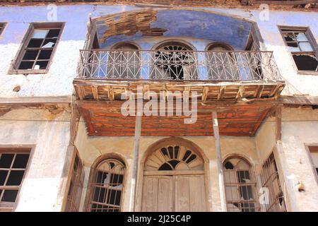 Front of an old vintage historical traditional abandoned stone and wood house with broken glasses, rounded bay windows and balcony. Stock Photo