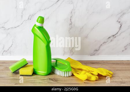 Cleaning supplies against marble wall. Copy space. Liquid toilet cleaner bottle, plastic brush, foam sponges and rubber gloves on the shelf. Stock Photo