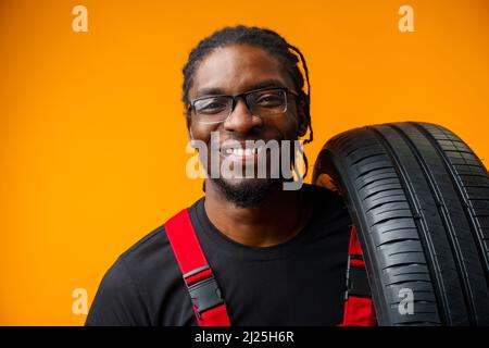 African american car service worker with car tyre against yellow background Stock Photo