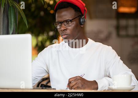 Concentration black hipster male in headphones, eyewear studying or working remotely on computer Stock Photo