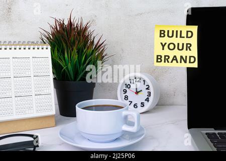 Build your brand typed on yellow paper stick on top of computer screen with other accessories. Stock Photo