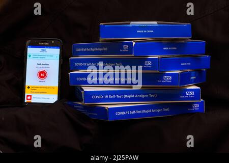 NHS Covid-19 lateral flow test kit boxes / rapid lateral flow antigen coronavrus test kits with the NHS test and trace app showing self isolation Stock Photo