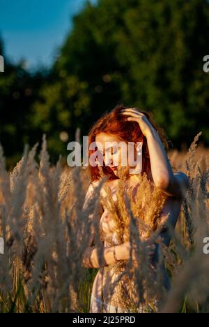 red-haired beautiful girl sits with her back in black, long dress in the grass Stock Photo