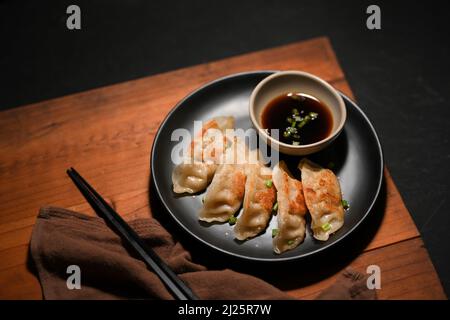 Traditional Chinese food cuisine, Fried dumplings or Gyoza served with special homemade sauce on a wood table with brown napkin and chopstick. Stock Photo