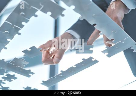 image of a businessman collecting puzzle pieces on an office desk. Stock Photo