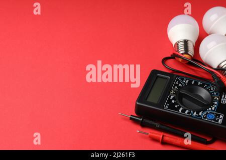 Multimeter and energy saving bulbs on red background Stock Photo