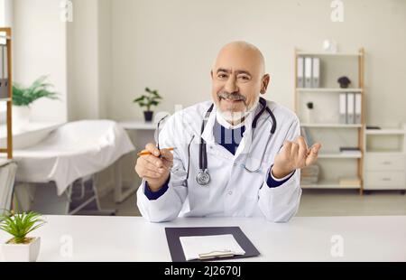 Senior online doctor sitting at desk and giving telemedicine consultation via video call Stock Photo