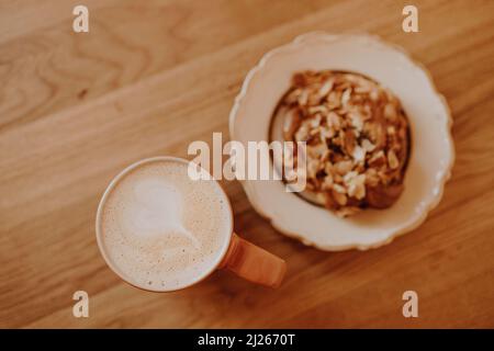 A cup of coffee and a fragrant bun on a wooden table in a city cafe Stock Photo