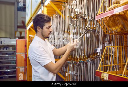Male customer at shelf in hardware store chooses stainless steel plumbing hoses. Stock Photo