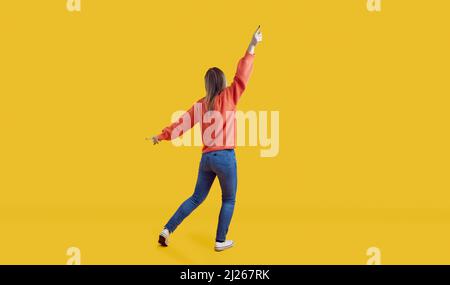 Full body back view of cheerful young woman dancing and having fun in yellow studio Stock Photo