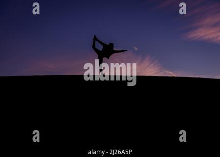 A silhouette of a female ballet dancer posing on a dark purple sky background Stock Photo