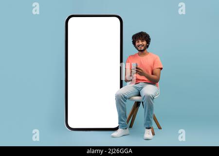 Cheerful curly eastern guy enjoying newest mobile app Stock Photo