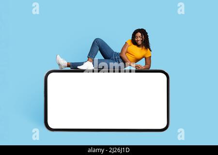 Pretty african american woman laying on big cellphone, mockup Stock Photo