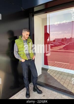 Handsome young man model in green gilet and black boots posing next to black wall in the old town. Morocco Stock Photo