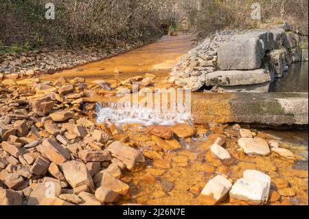 Orange iron oxide staining in stream entering River Neath at Abergarwed. The source is water discharging from an abandoned coal mine. Stock Photo