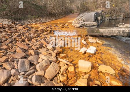 Orange iron oxide staining in stream entering River Neath at Abergarwed. The source is water discharging from an abandoned coal mine. Stock Photo