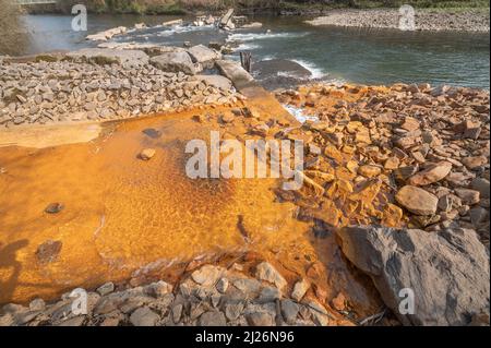 Orange iron oxide staining in stream entering River Neath at Abergarwed. The source is water discharging from an abandoned coal mine. Stock Photo