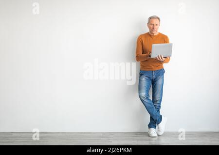 Confident mature man using laptop leaning on wall Stock Photo