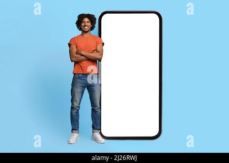 Confident black guy posing by big smartphone with empty screen Stock Photo