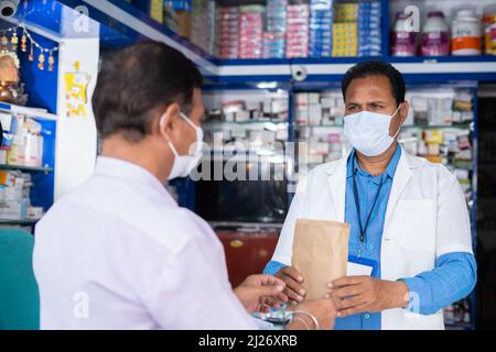 customer purchasing medicines from pharmacist while both in medical face mask at retail store during covid-19 coronavirus pandemic - concept of Stock Photo