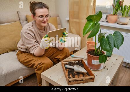 Woman gardener holds an Apple iPad tablet in her hands for online learning on plants. Blogger shoots videos and photos of home gardening for an online Stock Photo